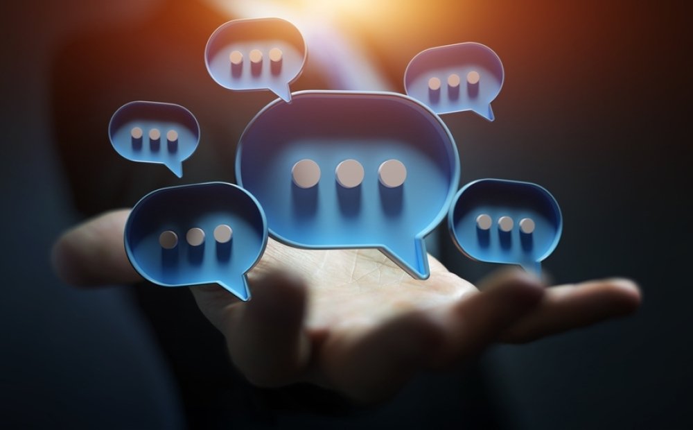 Businessman in dark using digital blue speech bubbles talk icons. Minimal conversation or social media messages floating over user hand. 3D rendering