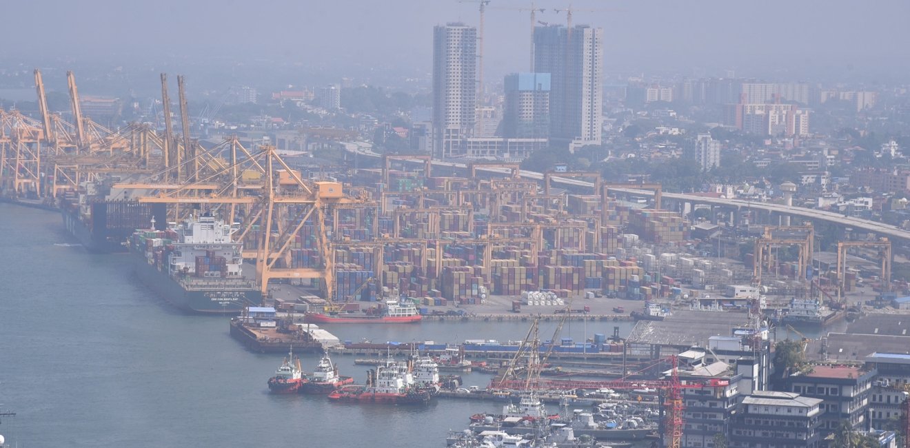 An aerial view of a port with cranes, ships, and skyscrapers.