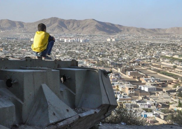 A boy sits on a ledge overlooking Kabul