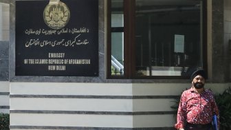 A man stands outside a building with a sign that reads Embassy of the Isalamic Republic of Afghanistan, New Delhi