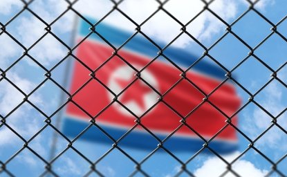 A blurry image of the flag of North Korea behind a chain link fence.