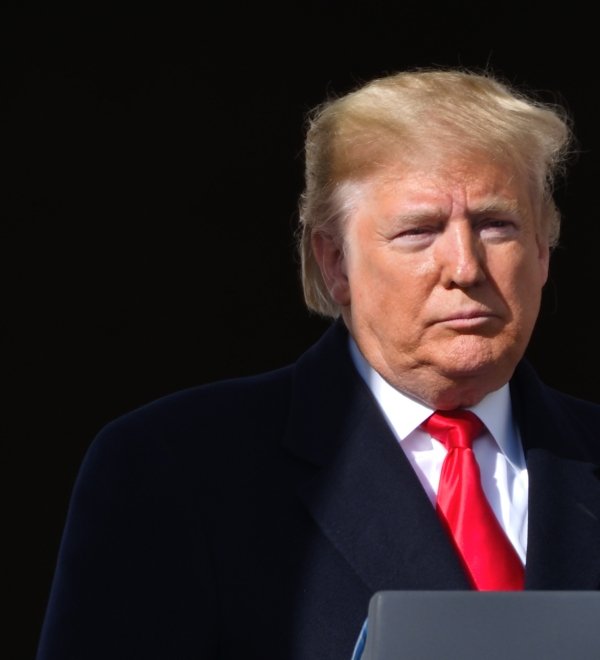 Donald Trump stands silently at a microphone, part of his face in shadow