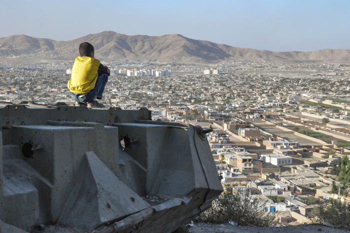KABUL, AFGHANISTAN 2012: Boy sitting on Destroyed Tank on the hills over Kabul City in Afghanistan