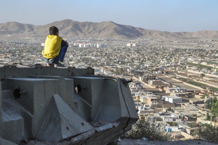 A boy sits on a ledge overlooking Kabul