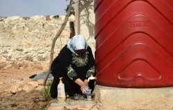 A housekeeper from Northern Syria washes dishes with water from a tank installed by OXFAM