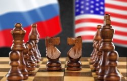 A chess board is set up with two knights facing each other, Russian and U.S. flags in the background.
