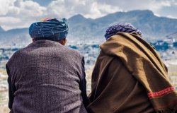 Two men sit with their backs to the camera, looking out at the Afghan mountains.