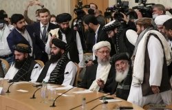 A group of Taliban officials sitting at a conference table with press behind them.