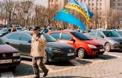 Crimean Tatar man with big beard and traditional cap walks on the city's street with Crimea Tatars and Ukrainian flags. 