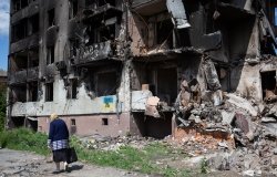 old woman walks past apartment building destroyed by the Russian army as a result of Russia's invasion of Ukraine in Borodianka, Ukraine