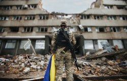 Ukrainian military woman with the Ukrainian flag in her hands on the background of an exploded house. 