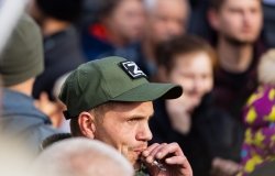 Man in crowd smoking a cigarette and wearing a hat in support of the special military operation